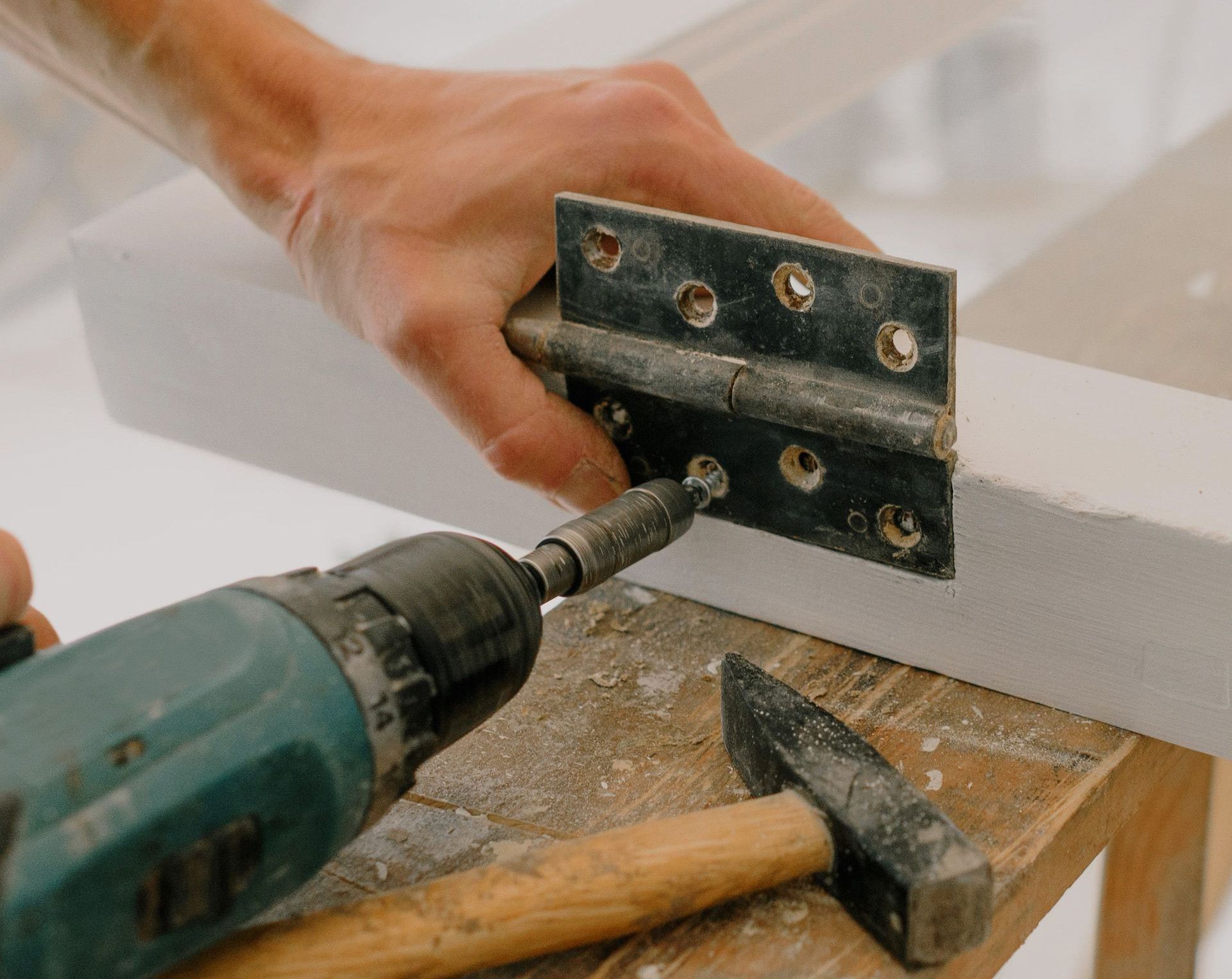 Crop unrecognizable craftsman attaching metal hinge with modern screwdriver on wooden window frame located on wooden board during renovation works