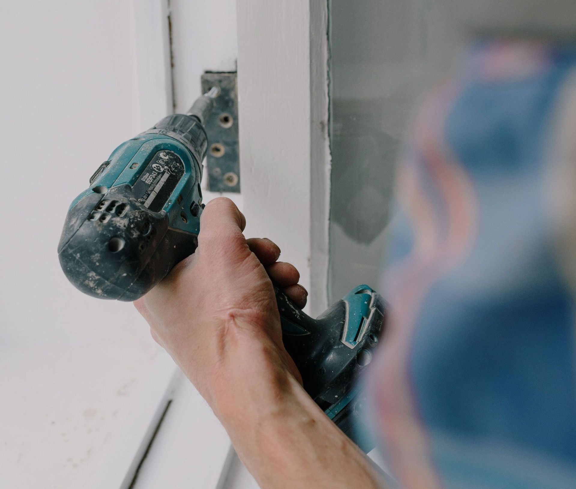Crop bearded guy installing new wooden window with contemporary screwdriver and metal hinge during renovation process in apartment